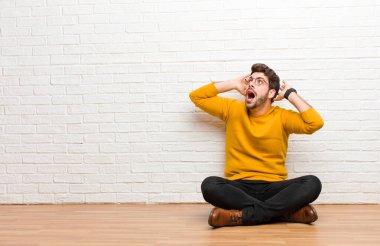 Genç yakışıklı adam tuğla duvar dokusuna karşı evde oturuyor.