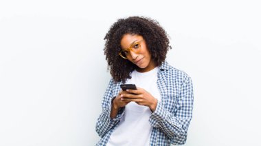 Beyaz duvarda akıllı telefonu olan genç, güzel siyah bir kadın.