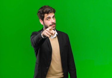 Genç işadamı kameraya tatmin olmuş, kendine güvenen, dostça gülümseyen yeşil arka planda seni seçiyor.