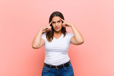 Ciddi ve konsantre görünümlü genç, güzel İspanyol kadın, pembe duvara karşı zorlu bir sorun düşünüyor ve beyin fırtınası yapıyor.