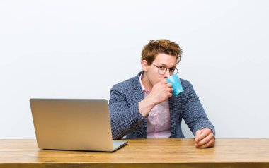 Genç kızıl saçlı işadamı masasında sıcak bir kahve bardağıyla çalışıyor.