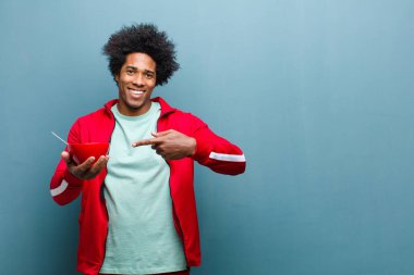 Mavi grunge duvarına karşı elinde kahvaltı kasesi olan genç siyah bir adam.