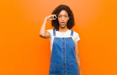Genç, güzel siyahi kadın şaşırmış, ağzı açık, şok olmuş, turuncu duvara karşı yeni bir düşünce, fikir ya da konsept keşfediyor.