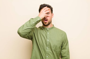 Genç yakışıklı adam şok olmuş, korkmuş ya da korkmuş görünüyor. Yüzü elle kaplanmış ve parmaklarının arasından gizlice bakıyor.