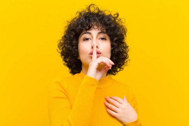 Genç ve güzel afro kadın ciddi görünüyor ve parmaklarını dudaklarına bastırıp sessizlik ya da sessizlik talep ediyor, sır saklıyor.