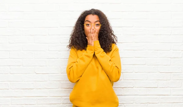 young black woman feeling worried, upset and scared, covering mouth with hands, looking anxious and having messed up against brick wall