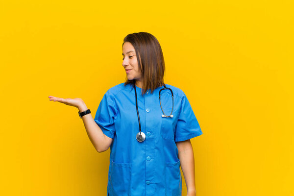 feeling happy and smiling casually, looking to an object or concept held on the hand on the side isolated against yellow wall