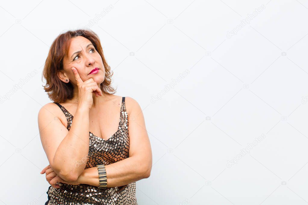middle age pretty woman with a concentrated look, wondering with a doubtful expression, looking up and to the side against white wall