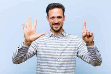 Genç yakışıklı adam gülümsüyor ve arkadaş canlısı görünüyor, altı ya da altıncı numarayı gösteriyor, eli önde, geri sayıyor.