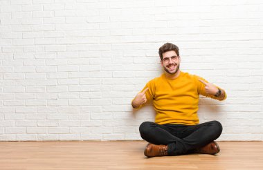 Genç yakışıklı adam tuğla duvar dokusuna karşı evde oturuyor.