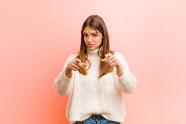 Genç ve güzel bir kadın kameraya hem parmaklarını hem de suratını göstererek pembe arka plana karşı görevini yapmanı söylüyor.