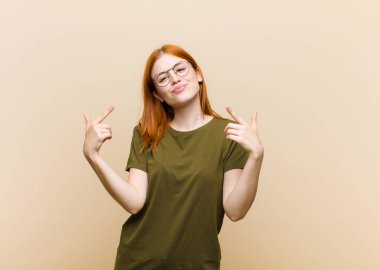 Genç kızıl saçlı kötü tavırlı güzel bir kadın gururlu ve agresif görünüyor, yukarıyı gösteriyor ya da elleriyle alay işareti yapıyor.