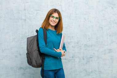 Kollarını kavuşturup kameraya gülümseyen genç bir kız öğrenci ve mutlu, kendinden emin, tatmin olmuş bir ifade.