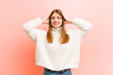 Genç, güzel bir kadın kendini stresli, endişeli, endişeli ya da korkmuş hissediyor. Elleri başının üstünde, pembe arka planda hata yaparken panikliyor.