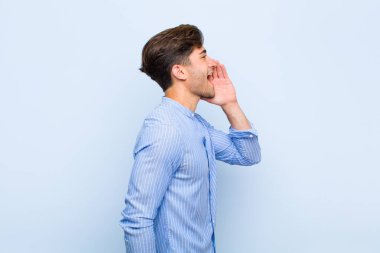 Genç yakışıklı profil görüntüsü, mutlu ve heyecanlı görünüyor, bağırıyor ve mavi arka planda yer almak için çağırıyor.