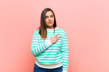 Genç, güzel İspanyol kadın mutlu, pozitif ve başarılı hissediyor. Göğsünde V şeklinde eller yapıyor. Pembe duvara karşı zafer ya da barış gösteriyor.