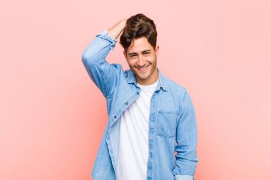 Genç ve yakışıklı bir adam pembe arka planda neşeli, mutlu, dostane bir gülümsemeyle güler.