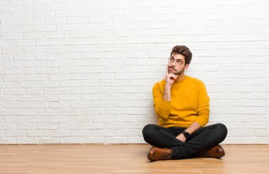 Genç yakışıklı adam tuğla duvar dokusuna karşı evde oturuyor.