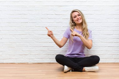 Genç sarışın güzel kadın mutlu bir şekilde gülümsüyor ve her iki elinde fotokopi uzayında nesne gösteriyor.