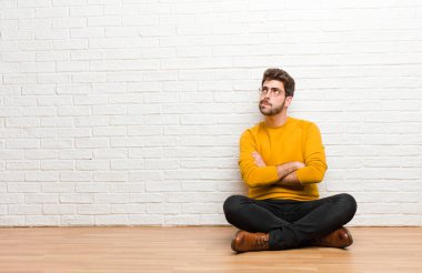 Genç yakışıklı adam tuğla duvar dokusuna karşı evde oturuyor.