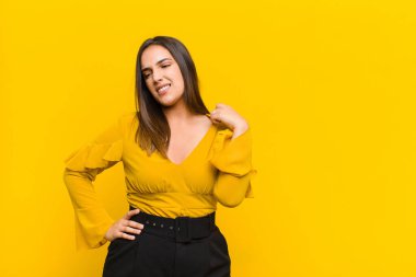 Genç, güzel bir kadın kendini stresli, endişeli, yorgun ve hayal kırıklığına uğramış hissediyor. Boynunu çekiştiriyor. Turuncu duvarda izole edilmiş bir sorun yüzünden hayal kırıklığına uğramış görünüyor.