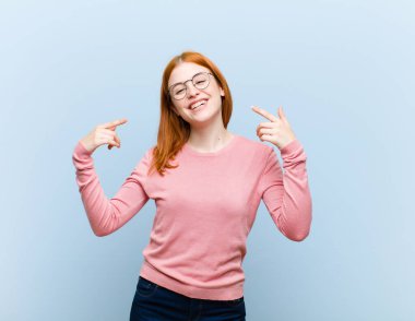 Genç kızıl saçlı güzel bir kadın, kendine güvenerek gülümsüyor. Geniş bir gülümseme, pozitif, rahat, tatmin olmuş bir tavır sergiliyor.