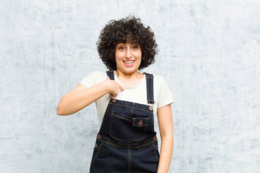 Genç, güzel afro kadın mutlu, gururlu ve şaşırmış görünüyor, neşeli bir şekilde kendini gösteriyor, kendinden emin ve yüce hissediyor.
