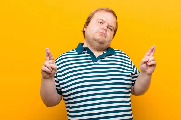 Genç Iri Bir Adam Endişeyle Parmaklarını Çaprazlayarak Turuncu Duvara Karşı — Stok fotoğraf