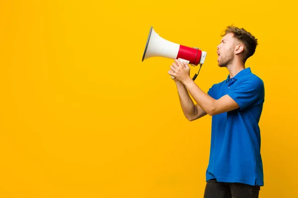 Jovem com um megafone contra fundo amarelo — Fotografia de Stock