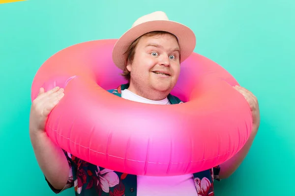 young big size man with a inflatable donut against flat wall