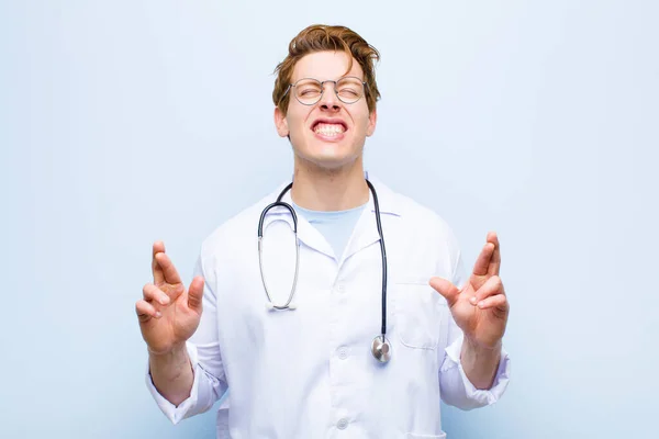 Joven Médico Cabecera Roja Sonriendo Ansiosamente Cruzando Ambos Dedos Sintiéndose —  Fotos de Stock