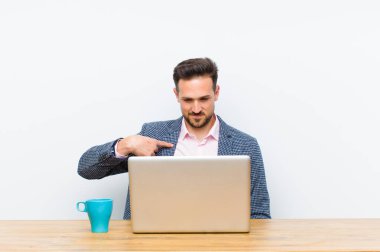 Genç ve yakışıklı işadamı neşeli bir şekilde gülümsüyor, aşağıya bakıyor ve göğsüne işaret ediyor.