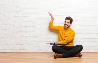 Genç yakışıklı adam tuğla duvar dokusuna karşı evde oturuyor.