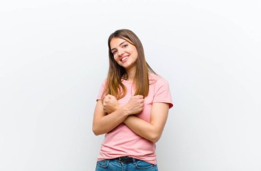 Genç ve güzel bir kadın, neşeli bir şekilde gülümsüyor ve kutluyor, yumruklarını sıkmış ve kollarını kavuşturmuş, mutlu ve pozitif hissediyor beyaz arka plana karşı.