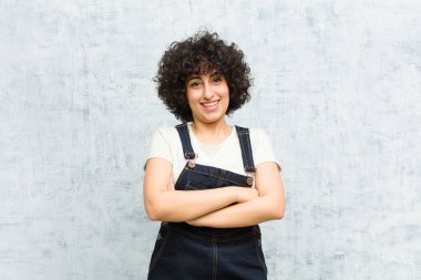 Genç, güzel afro bir kadın mutlu, gururlu ve tatmin olmuş görünüyor. Kollarını kavuşturup gülümsüyor.