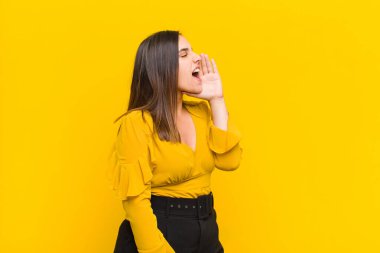 Genç ve güzel bir kadın profili, mutlu ve heyecanlı görünüyor, bağırıyor ve turuncu duvara karşı izole edilmiş bir şekilde kopyalama alanı istiyor.