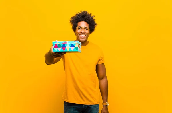 Jong Afrikaans amerikaans man met een gift box tegen oranje backgr — Stockfoto