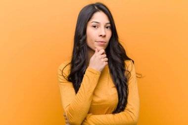 Genç, güzel, İspanyol bir kadın ciddi, kafası karışmış, kararsız ve düşünceli görünüyor. Seçenekler arasında veya kahverengi duvara karşı seçimler yapıyor.