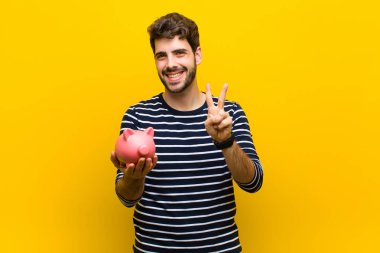 Genç yakışıklı bir adam kumbarasını turuncu sırt grubuna karşı tutuyor.