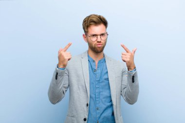 Kötü tavırlı genç işadamı gururlu ve agresif görünüyor, yukarı bakıyor ya da mavi arka planda ellerle alay ediyor.