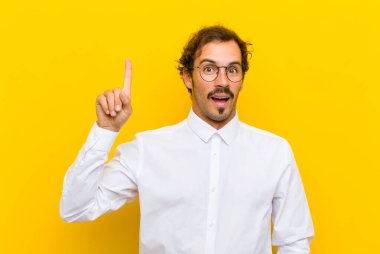 Genç yakışıklı bir adam bir fikri fark ettikten sonra mutlu ve heyecanlı bir dahi gibi hissediyor, neşeli bir şekilde parmağını kaldırıyor, eureka! turuncu duvara yaslan