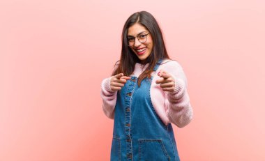 Genç, güzel bir kadın pozitif, başarılı, mutlu bir tavırla kamerayı işaret ederek, pembe arka planda elleri olan bir silah işareti yapıyor..