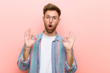 Delikanlı şok olmuş, şaşırmış ve şaşırmış hissediyor. Onaylıyor. Her iki elini de pembe arka planda tutuyor.