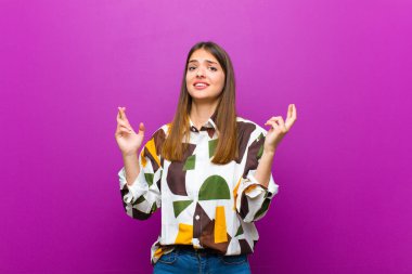 Genç ve güzel bir kadın endişeyle dua ediyor ve mor arka planda endişeli bir bakışla iyi şanslar diliyor.