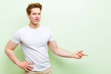 Genç kızıl saçlı yakışıklı adam mutlu ve neşeli hissediyor, gülümsüyor ve seni selamlıyor, dostça bir jestle içeri davet ediyor.