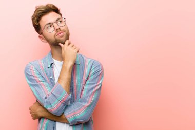 Genç adam düşünceli, meraklı ya da hayal kuruyor, hayal kuruyor ve pembe arka planda boşluğu kopyalamaya çalışıyor.