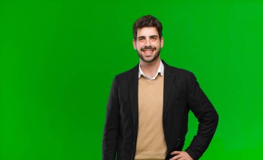 Genç işadamı mutlu bir şekilde gülümsüyor, kendine güvenen, olumlu, gururlu ve dost canlısı bir tavırla yeşil arka plana karşı.