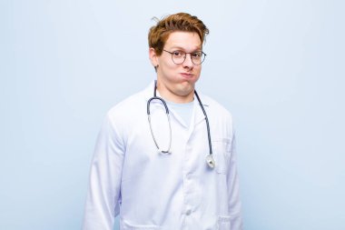 Aptal, çılgın, şaşkın bir ifadeyle genç, kızıl saçlı doktor. Yanakları şişmiş, içi doldurulmuş, şişman ve mavi duvarda yemek dolu.