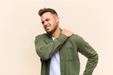 Genç İspanyol bir adam yorgun, stresli, endişeli, hayal kırıklığına uğramış ve depresyonda, izole edilmiş arka planda sırt ya da boyun ağrısı çekiyor.