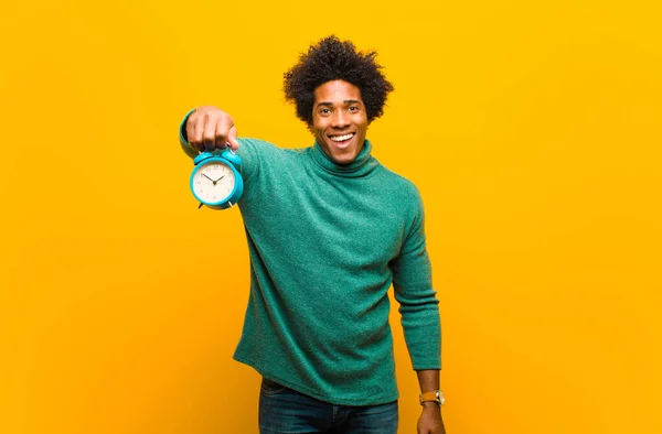 Jovem afro-americano homem com um despertador contra laranja ba — Fotografia de Stock